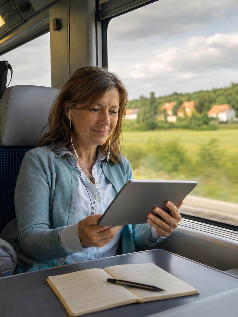 Frau lernt im Zug mit Tablet und Notizbuch Ungarisch online